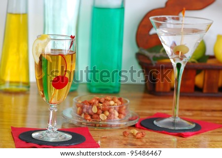 Spicy peanuts and mixed drinks on wooden bar at Happy Hour in Local Pub with colorful bottles in background.