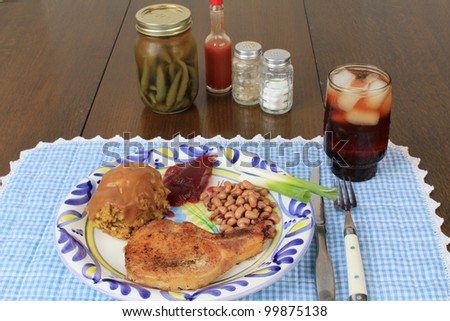 Typical country setting of pork chop and dressing with black-eyed peas and cranberry sauce.  Setting is on old table with bottles of pickled pepper sauce, hot sauce and salt and pepper.