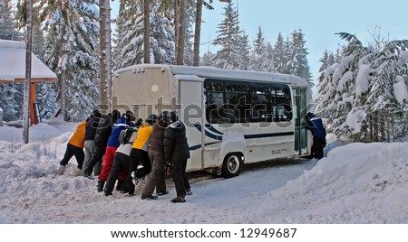 Group of people pushing a bus in the snow