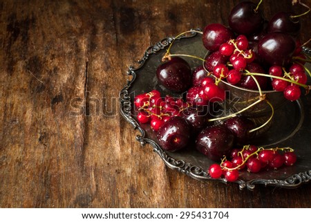 cherry with red currants in a bowl and a metal plate in oriental style on a background of wood