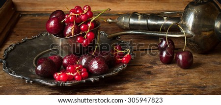 cherry with red currants in a bowl and a metal plate in oriental style on a background of wood