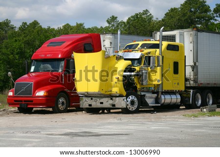 Two 18-wheeled trucks, one yellow, one red, stopped for maintenance. Yellow truck\'s hood is open.