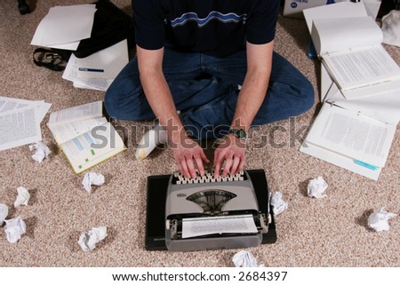 A person surrounded by reference materials works at  a typewriter.