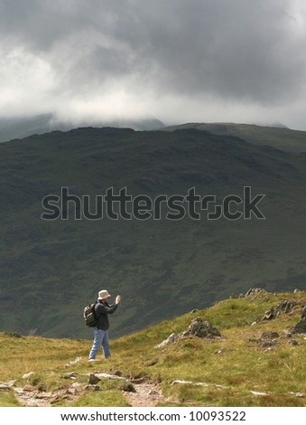 A hiker taking a photograph of the view on a rainy day in the mountains