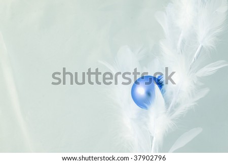 A small blue christmas bauble on pale blue feather background