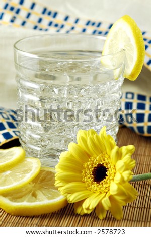 Glass of water with lemon set with bamboo mat, vintage linen, daisy and lemon slices