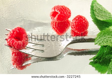 Fresh chilled raspberry on a fork with mint on a reflective background -- shaped like a long-stem rose