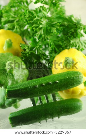 Variety of fresh summer squash pierced with a fork on a reflective watery mirrored background
