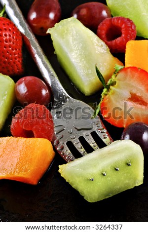 Variety of fresh fruit prepared for a salad on a watery black plate