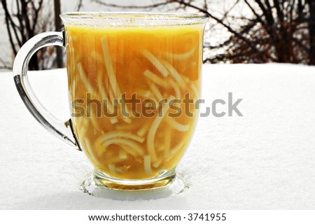 Steaming hot cup of chicken noodle soup on a cold snowy day