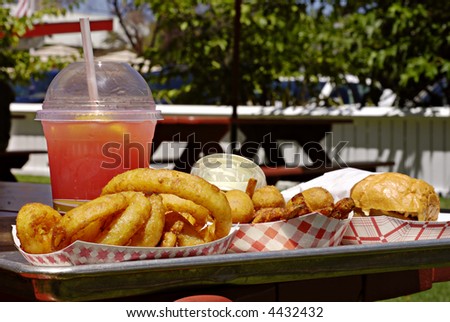 Fast food picnic lunch with onion rings, mini corn dogs, sweet potato French fries, and an ahi burger with a cup of watermelon lemonade