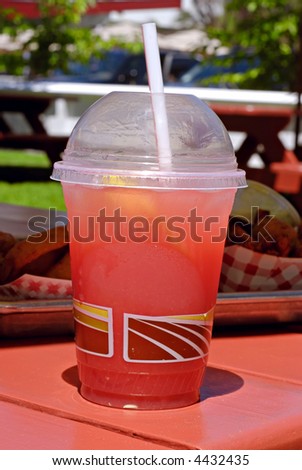 Plastic drink cup filled with fresh watermelon lemonade on an outdoor picnic table with lunch