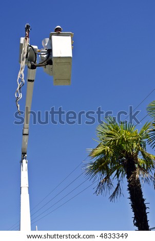A utility company electrician stands in a bucket boosted by a boom crane as it maneuvers towards power lines during installation of a new power pole