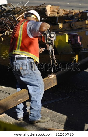 Electric company worker drills a hole in a cross beam for a new power pole