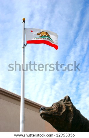 Bronze statue of a bear looking skyward at the California State flag with the Golden State Bear