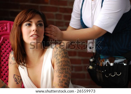 stock photo : Hairstylist works on young tattooed model's hair during photo