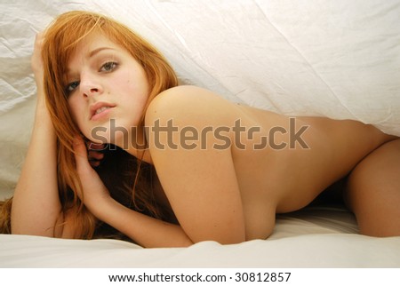 Young naked woman hiding under white bed sheets