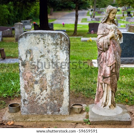 Weathered headstone with blank copyspace next to vintage statue of Jesus