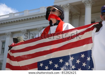 SACRAMENTO, CALIFORNIA - FEBRUARY 26: An unidentified protester with mouth covered holds upsdie-down flag at the California State Capitol during rally in Sacramento, California, on February 26, 2011