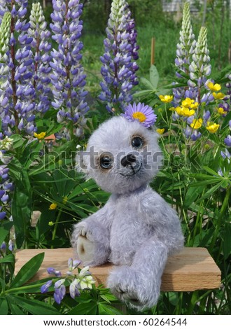 Handmade, the sewed toy: teddy-bear Chupa on a little board among flowers lupine and buttercups