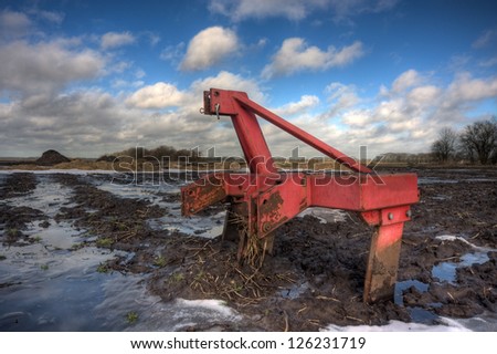 Red harrow, left behind on a muddy field in winter