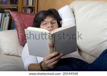 Woman laying on a couch reading a book (selective focus on a book)