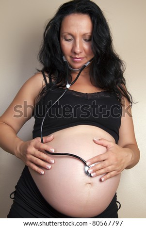 A happy pregnant lady with a stethoscope listening to a her own belly