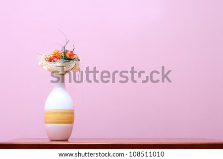 Ceramic vase with dry flowers on wooden table against purple wall