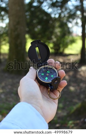 Male hand holding compass in forest, vertical orientation
