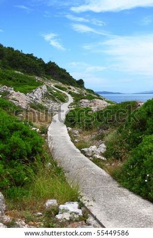 Paved walkway winding through rocky mediterranean landscape near the sea, island Losinj, Croatia