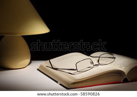 Reading glasses resting on top of open book next to night lamp