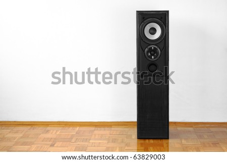Single floor-standing loudspeaker on hardwood against white wall