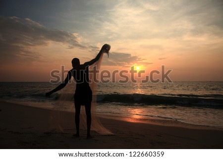 Silhouette of a fisherman works with his net during sunset