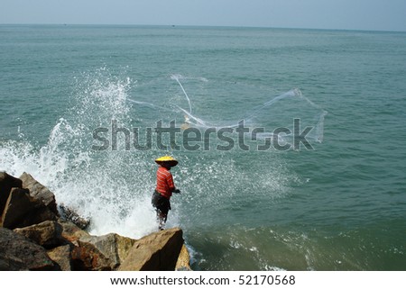 A fisherman throwing out fishing net in to  sea.