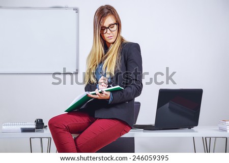Businesswoman writing notes and sitting on desk