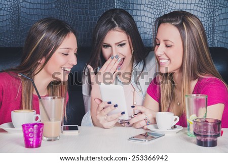 Three young girls laughing while looking at the mobile phone in a cafe
