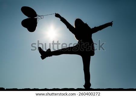 Girl lifting leg and arms in the air while holding balloons