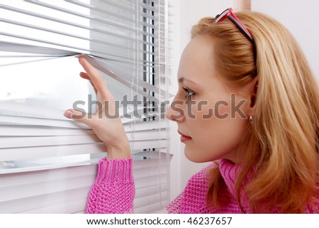 girl looks out the window half open blinds