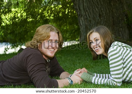 Young Married couple laying down on the grass holding each others hand