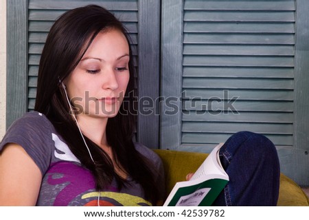 Teen Girl Reading a Book in a Chair while Listening to Music