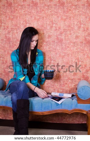 Beautiful  Teenager Girl Drinking Coffee at Home while Reading a Magazine
