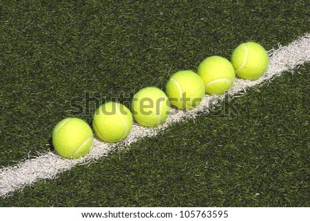 Yellow tennis balls lays in-line on court with green synthetic grass