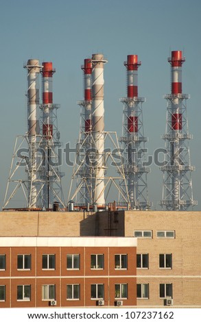 Industrial building and many smoke pipes after it over blue sky