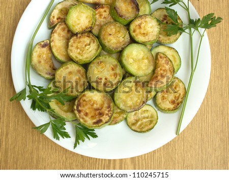 Fried zucchini slices with parsley on a white plate close up