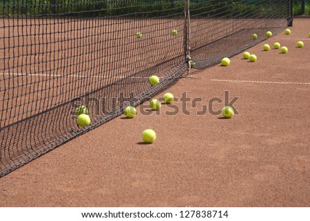 Ground court with net and many yellow tennis balls