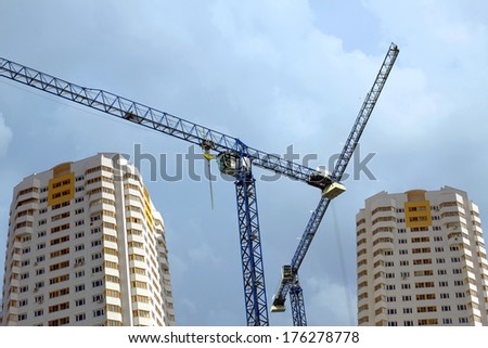 Two Big hoisting tower cranes and high constructed buildings over cloudy sky