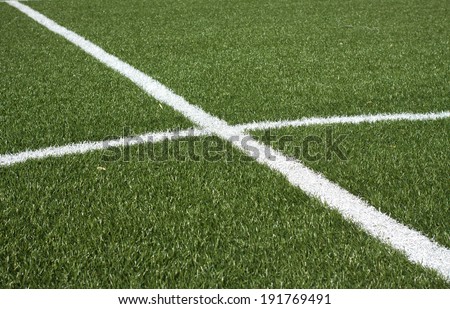 The center part of a soccer field with green synthetic grass and white lines on it closeup