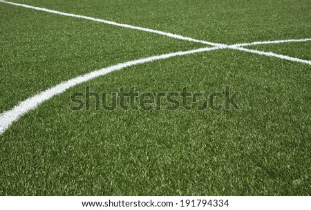 The center part of a soccer field with green synthetic grass and white lines on it horizontal view closeup