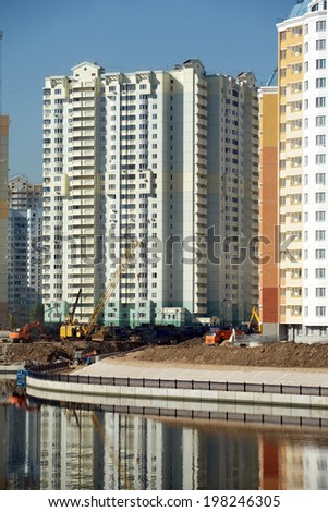 Cityscape with new modern buildings construction near river over clear blue cloudless sky in summer day, vertical photo