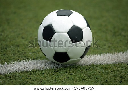 Classic ball for playing soccer in white with black accents on artificial turf line, close-up view